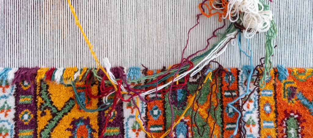 Colourful custom rug being hand knotted on a traditional vertical loom in Jaipur, India